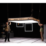 Two Gaffers handling a Godox KNOWLED AM1600R-48K 4'x8' Inflatable RGB LED Light Mat suspended from the a ceiling rig in s movie studio