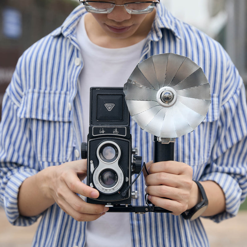 Godox FB01 Camera Mount Flash Bracket with a LUX Master flash and an old twin-lens reflex camera mounted to it being held by a photographer