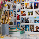 Collection of photos on a wall with makeup brushes and books in the foreground.