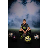 A you boy wearing football attire in front of a Sweep Sports Stadium Lighting Backdrop  sitting on a football