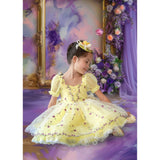 A young girl in a yellow dress with floral decorations, sitting on a Sweep Fine Art Flower Gold Frame Purple Curtain Backdrop