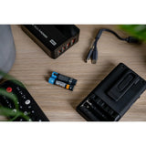 Two Newell USB-C Rechargeable  batteries on a wooden table surrounded by electronic devices