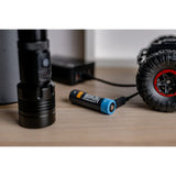 The Newell 18650 USB-C Rechargeable battery with a Black torch, and a tyre from an RC car on a wooden surface with a blurred background