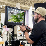 A person using an Osee Mega 22S4  21.5 Ultimate Multi-camera production monitor in an indoor setting with plants and furniture.