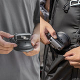 Two hands holding a black and gray device, one close-up and one with a person wearing a jacket.