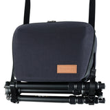 A Vanguard VEO CITY CB29 6 Litre Cross Body Camera Bag with a brown leather logo patch, shown with a folded black tripod resting underneath on a white background.