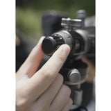 A close-up of a person's hand adjusting the MH38A Windmill Panoramic Head, with a blurred outdoor background.